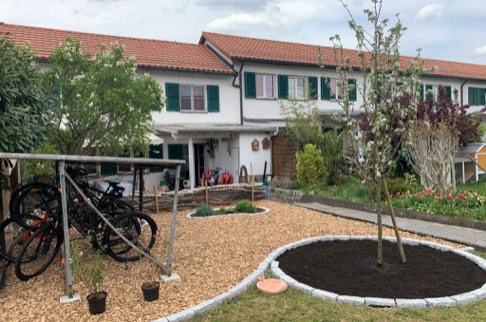FHG am Hörnli, Reihenhaus mit rotem Ziegeldach, Garten im Vordergrund mit Baum und Fahrradständer.