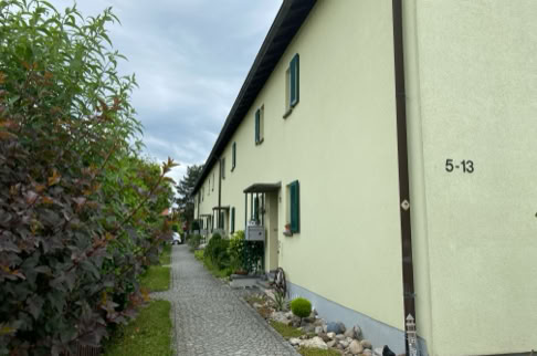 FHG am Hörnli, Reihenhaus mit gelber Fassade, grünen Fensterläden und einem gepflasterten Gehweg daneben.