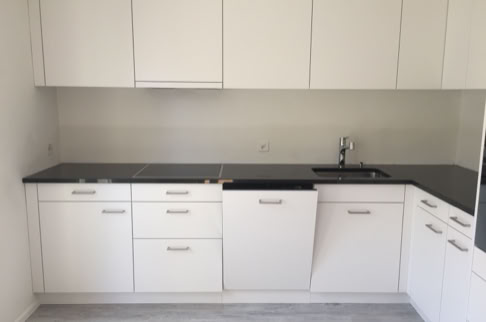 FHG am Hörnli, Weiße Einbauküche mit schwarzen Arbeitsplatten, mehreren Schränken und einer Spüle.