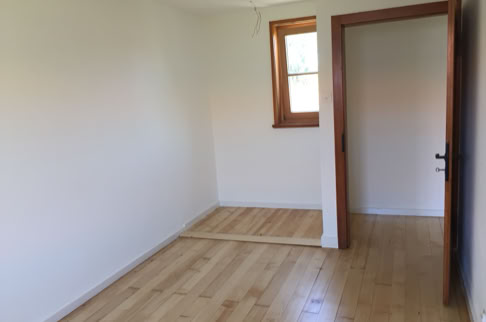 FHG am Hörnli, Leerer Raum mit Holzboden, weiß gestrichenen Wänden, einem Fenster und einer offenen Tür.