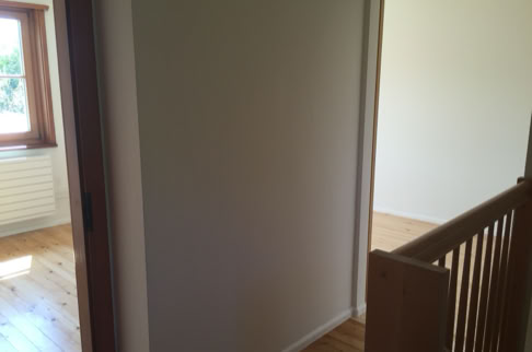 FHG am Hörnli, Flur mit Holzboden, einer Treppe mit Holzgeländer und zwei offenen Türen, die in helle Räume führen.